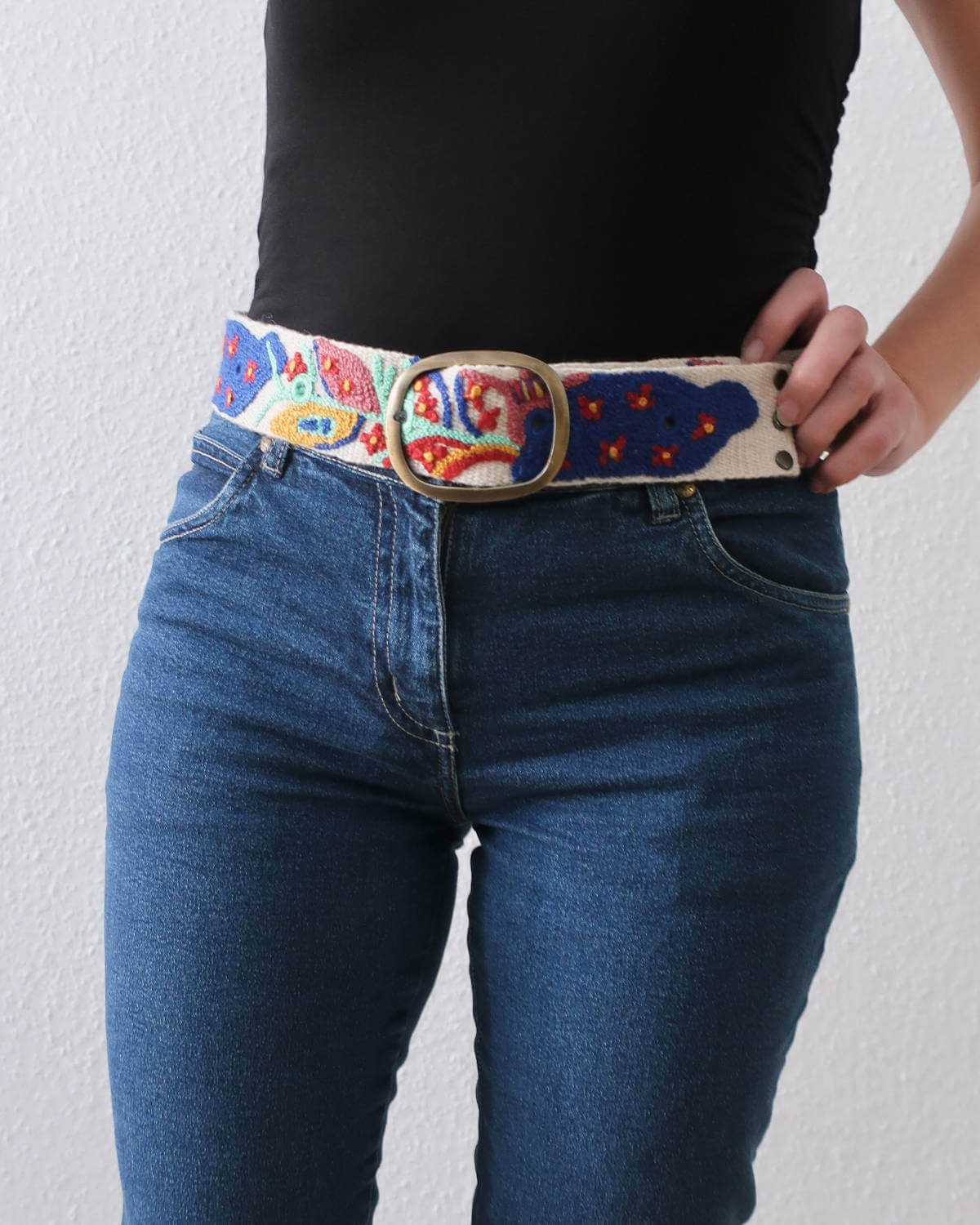 Ayni Ppacha Gürtel Piri Piri für Damen, in Peru aus Wolle bestickt mit bunt abstraktem Design, stilvoll kombiniert zu einer blauen Jeans.