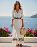 Model trägt den bestickten Ayni Ppacha Gürtel 'Ponsetia' als Taillengürtel über einem weißen, bestickten Maxikleid, mit Blick auf das Meer.