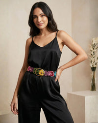 Model trägt den schwarzen, handbestickten Gürtel 'Aralia' aus 100% Schafwolle von Ayni Ppacha als eleganten Taillengürtel über einem schwarzen Satin-Jumpsuit.