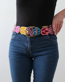 Ayni Ppacha Gürtel Aralia für Damen, in Peru aus Wolle bestickt mit bunten Blumen auf schwarzer Basis, stilvoll kombiniert zu einer blauen Jeans.