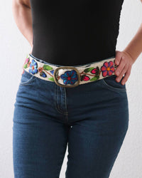 Ayni Ppacha Gürtel Ramo für Damen, in Peru aus Wolle bestickt mit bunten Blumen auf weißer Basis, stilvoll kombiniert zu einer blauen Jeans.