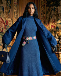 Model trägt den bestickten Gürtel 'Morera' mit Blätter-Muster als farbigen Akzent zu einem dunkelblauen Strickkleid und passendem Wollmantel im eleganten Winter-Look.