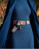 Layering-Inspiration: Der bestickte Wollgürtel 'Morera' blitzt unter einem offenen, dunkelblauen Wintermantel hervor und betont die Taille.