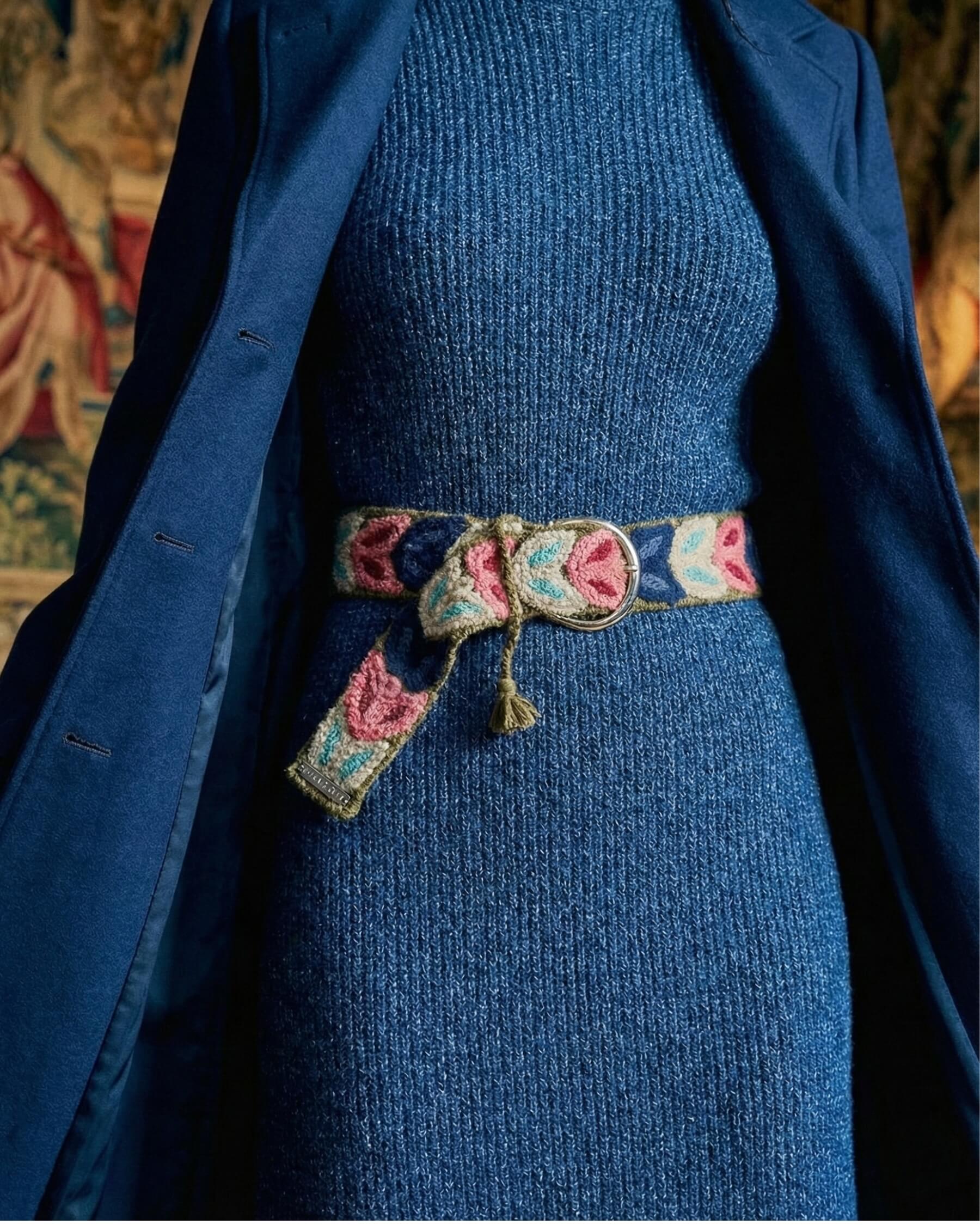 Layering-Inspiration: Der bestickte Wollgürtel 'Morera' blitzt unter einem offenen, dunkelblauen Wintermantel hervor und betont die Taille.