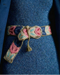 Der Ayni Ppacha Gürtel 'Morera' als Taillengürtel auf einem blauen Strickkleid getragen, wobei das rosa-blaue Blumenmuster einen schönen Kontrast bildet.