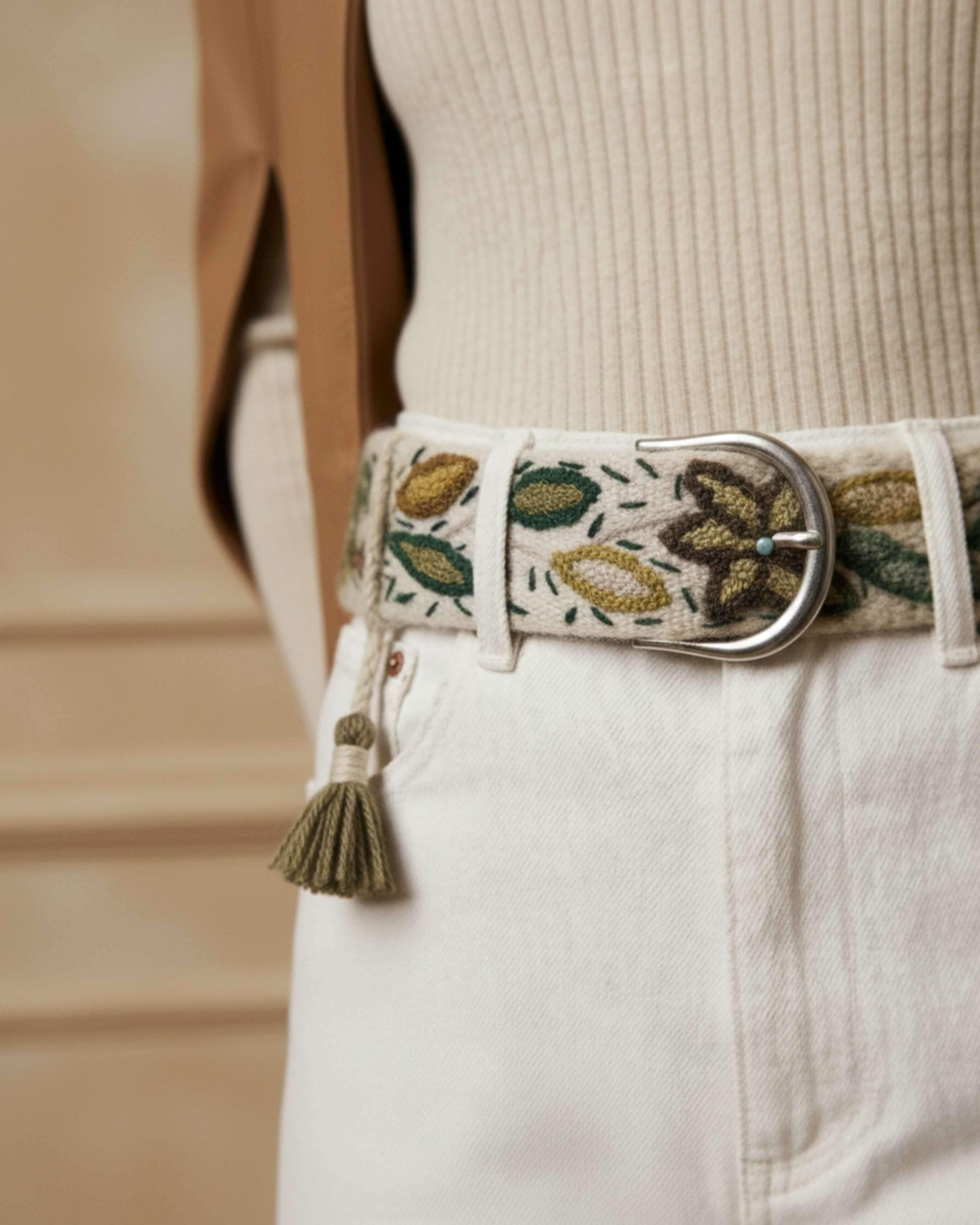 Extreme Nahaufnahme der Textur der 100% Schafwolle und der handgefertigten Stickerei des Gürtels 'Nolina', die die natürliche Haptik und die silberne Schnalle zeigt.