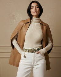 Model im eleganten "Quiet Luxury" Look trägt den cremefarbenen Ayni Ppacha Gürtel 'Nolina' mit olivgrüner Stickerei zu einer weißen Jeans, passendem Rollkragenpullover und einem Camel-Leder-Cape.