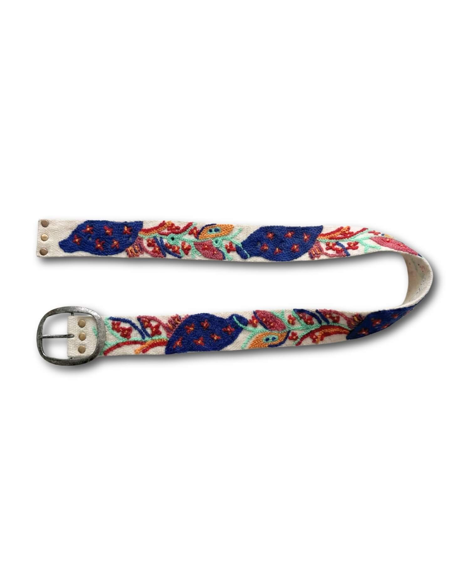 Ansicht des bestickten Gürtels 'Piri Piri' von Ayni Ppacha in geschwungener Form, die den Verlauf des bunten Blumenmusters (Blau, Rot, Türkis, Gelb, Rosa) auf dem wollweißen Wollstoff zeigt.